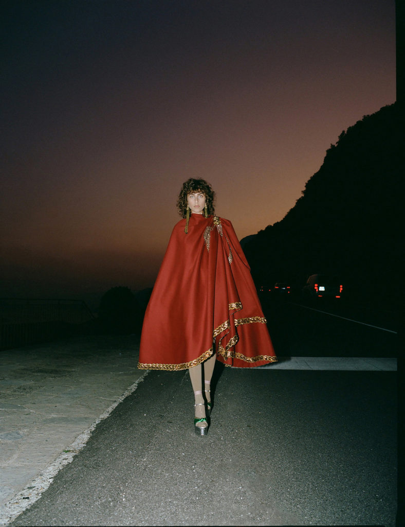 campagne Gucci representant une femme brune habillé d'une cape rouge marchant dans la pénombre
