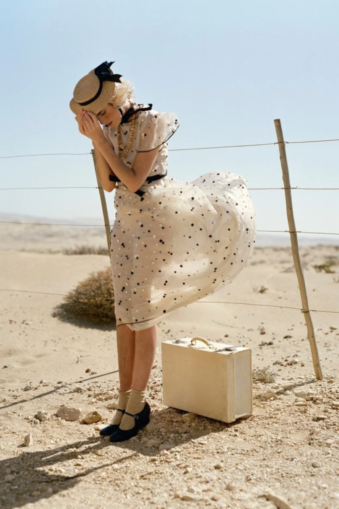 Femme en robe blanche et noire au milieu du desert avec une valise blanche