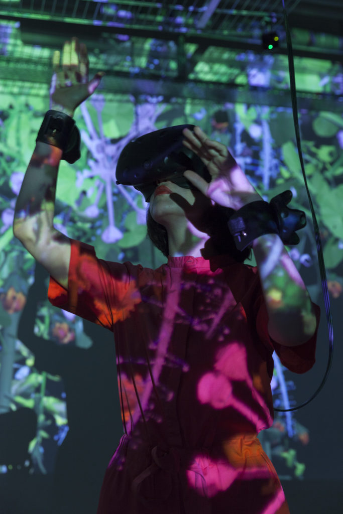 Photo d'une femme portant un casque de realité virtuelle devant une oeuvre de Mélanie Courtinat