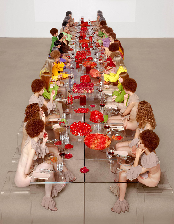 Mannequins nu.e.s ou habillé.e.s assis autour d'une table transparente recouverte d'aliments rougee
