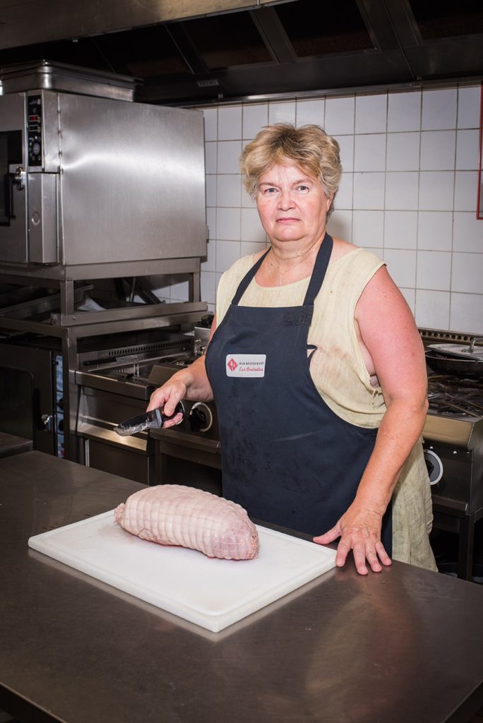 Femme blonde dans sa cuisine de routiers tenant un couteau au dessus d'un roti
