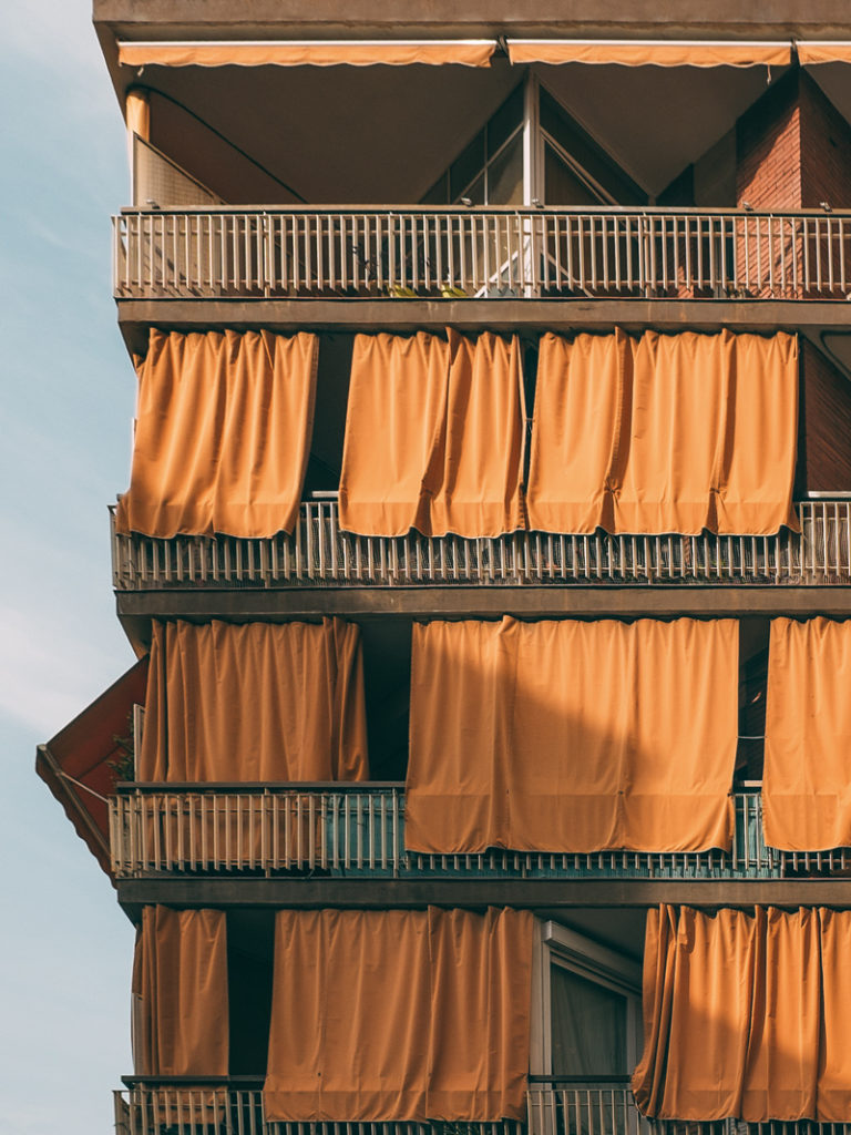 Façade d'immmeuble barcelonnais avec des rideaux orange qui volent