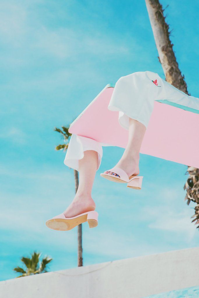 Jambes de femme habillée en bleu dépassant d'un plongeoir rose sur un fonod de ciel bleu et palmier