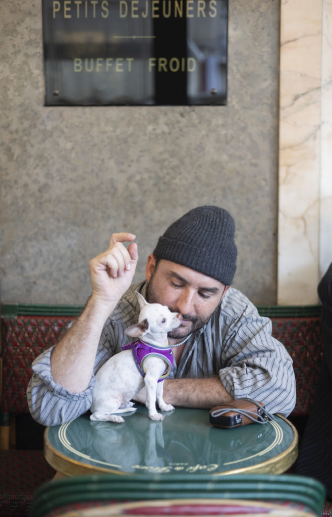 Portrait du photographe Rémi Ferrante portant un bonnet gris au café de Flore avec sa chienne Michelada